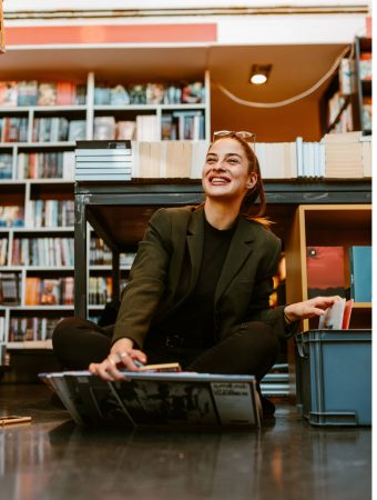 Portrait of smiling young brunette holding several vinyls while Portrait of smiling young brunette holding several vinyls while sitting on the floor at store. LPs gives whole different dimension to the music.